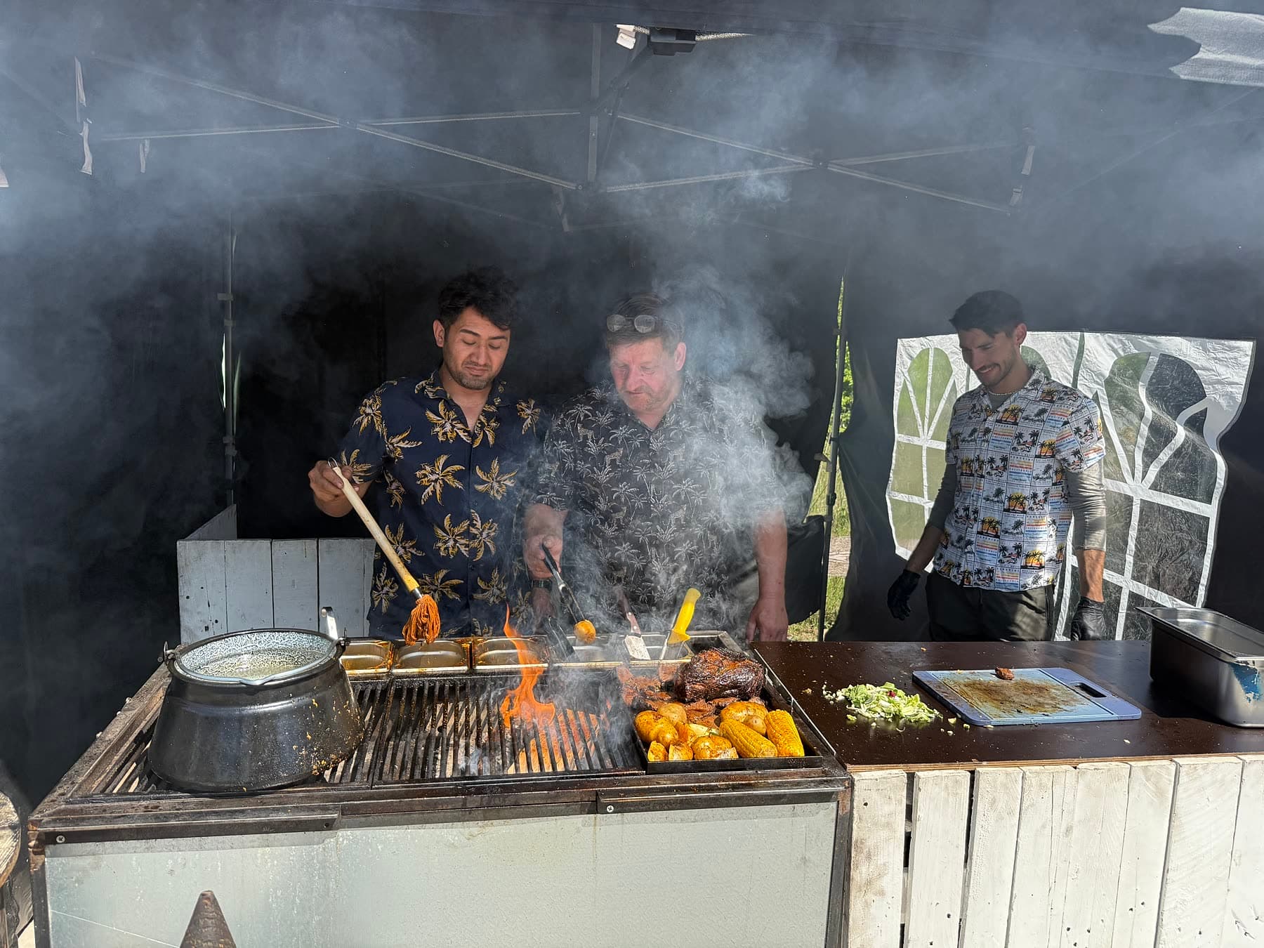 CARACAS Food-Artisten grillen Smoked Beef über offenem Feuer — Rauch steigt auf, Flammen lodern, Mais und Fleisch auf der Parrilla