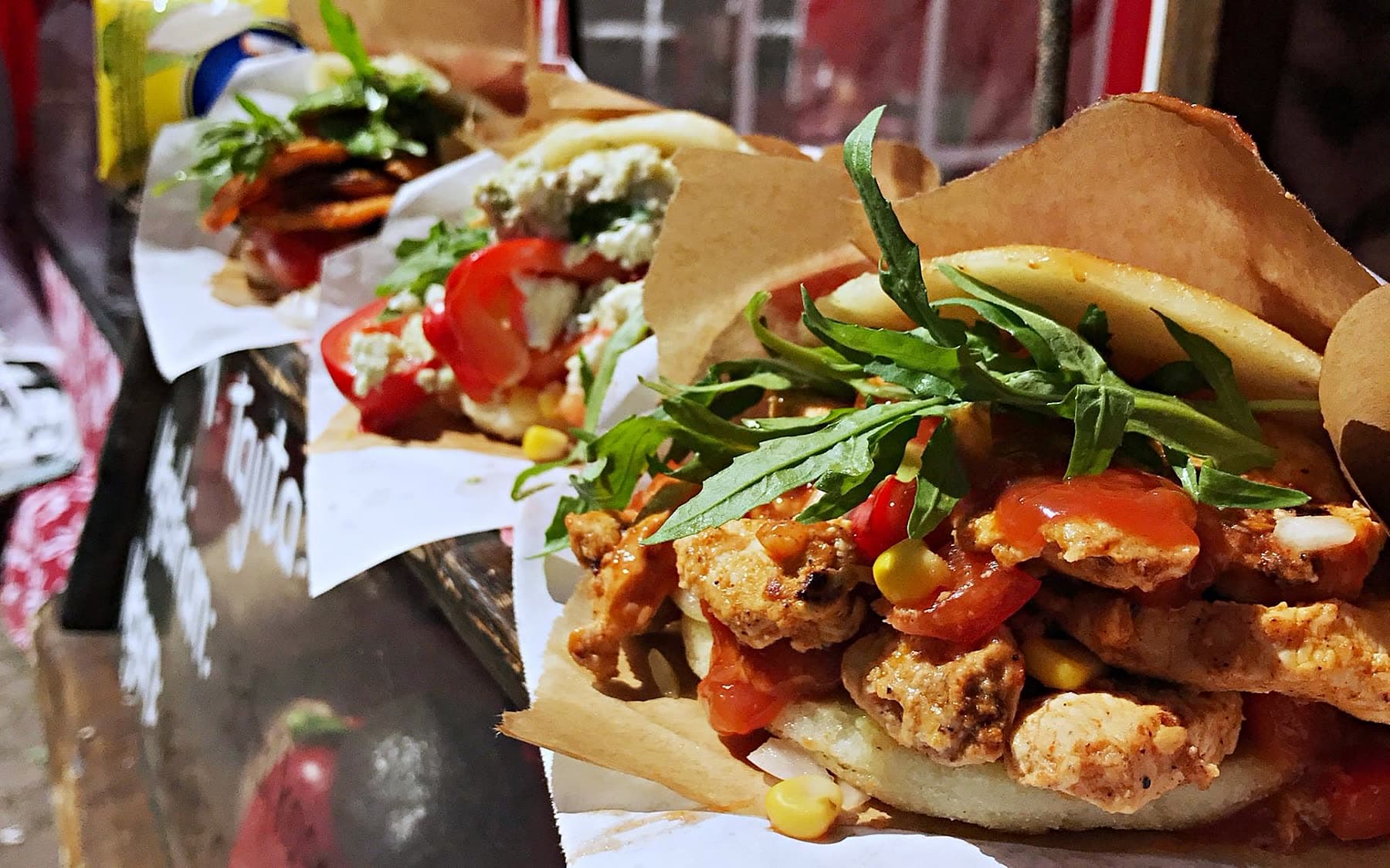 Drei Arepas in Reihe — glutenfreies Maismehl-Sandwich gefüllt mit Pulled Chicken, Tomaten, Rucola, Schafskäse-Avocado und Salsa