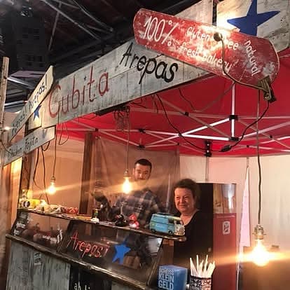 Cubita-Crew am Stand unter pinkem Zeltdach, warme Lichterketten-Atmosphäre