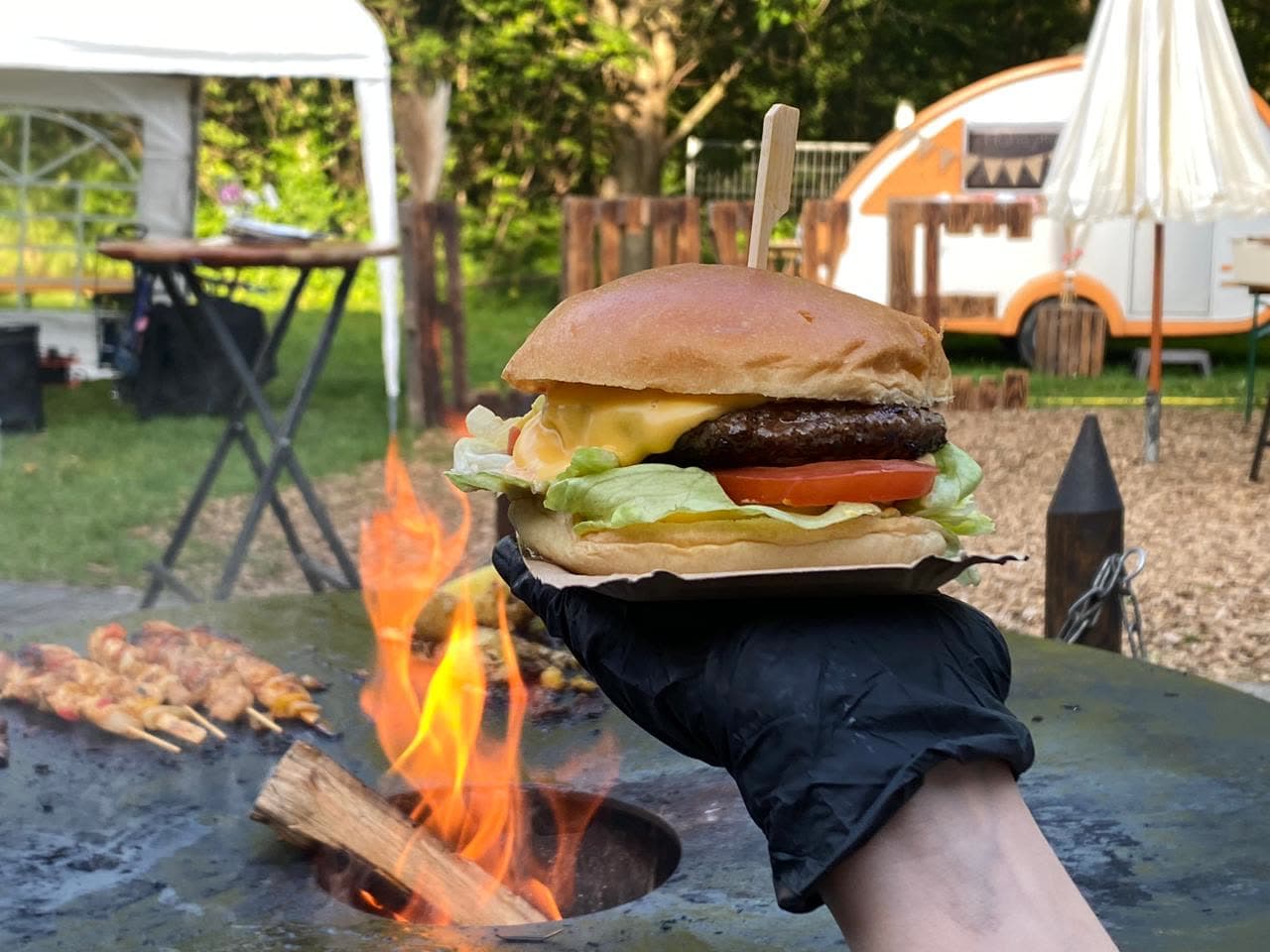Fire Smash Burger auf der Feuerschale mit Vintage-Hänger und Grillspießen im Hintergrund — typische Outdoor-Event-Kulisse