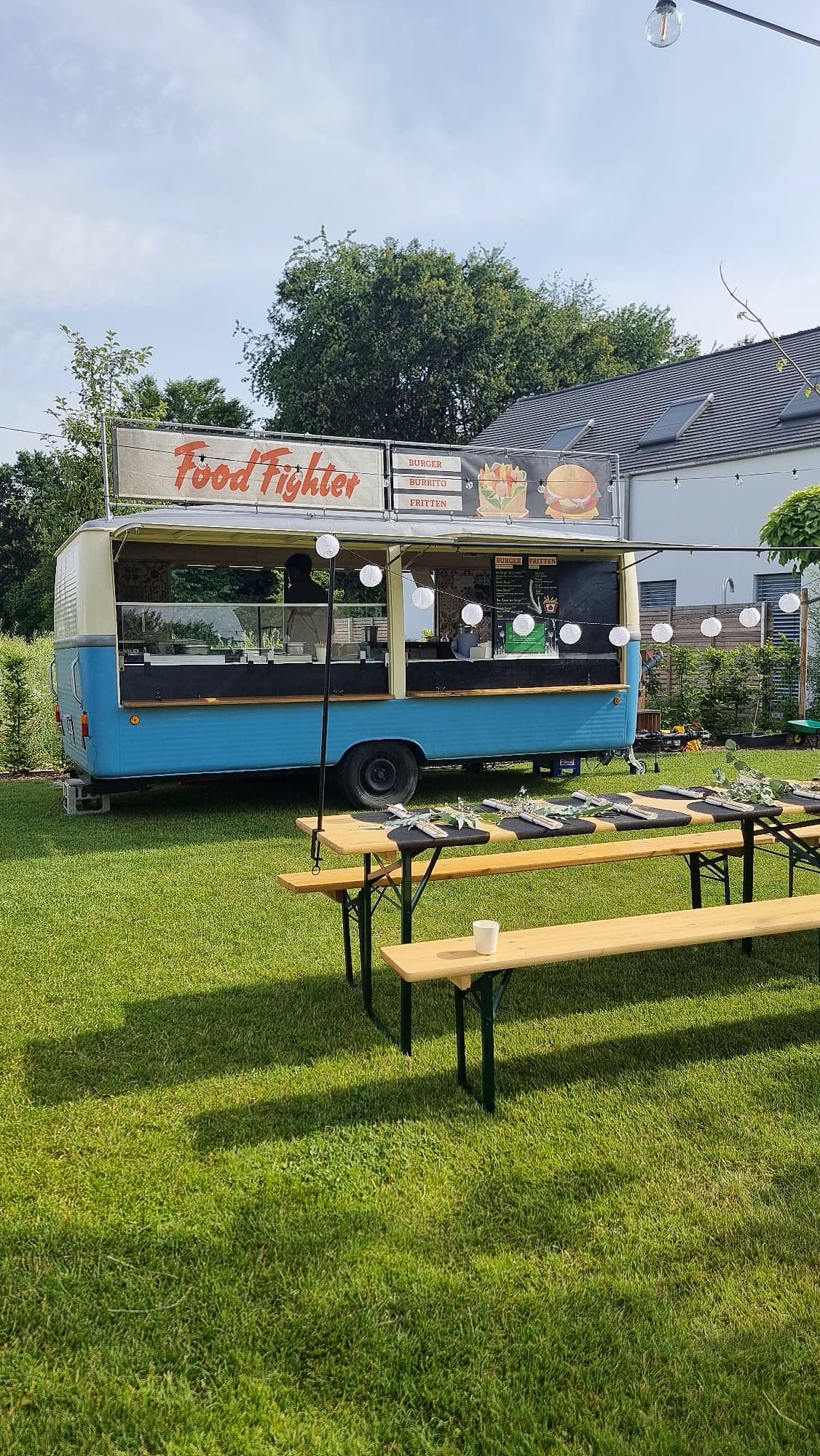 FoodFighter Vintage-Hänger auf einer Hochzeit — Lichterketten über Biergarten-Tischen mit Blumendeko, Garten-Setting